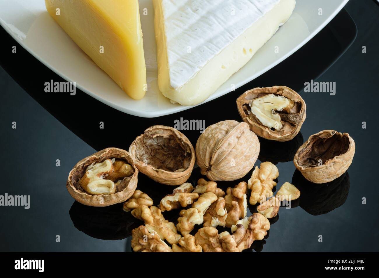 Walnüsse auf glänzendem schwarzem Hintergrund neben Parmesan und Brie-Käse. Stockfoto