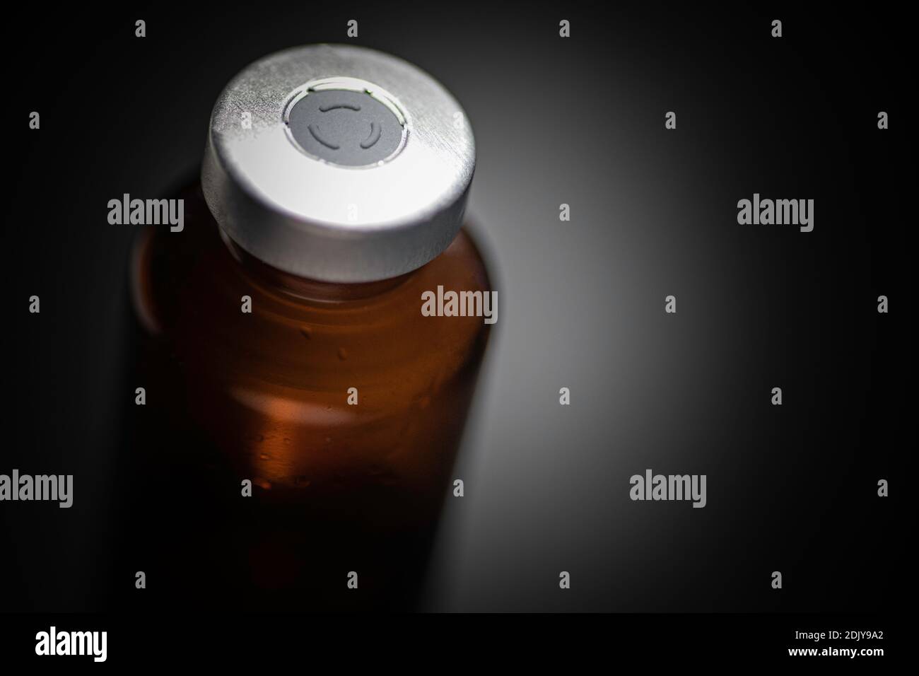 Eine Makroaufnahme mit selektivem Fokus einer bernsteinfarbenen Impfstoffflasche auf schlichtem schwarzen Hintergrund. Stockfoto
