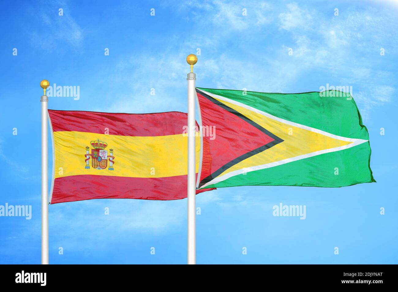 Spanien und Guyana zwei Flaggen auf Fahnenmasten und blau bewölkt Himmel Stockfoto
