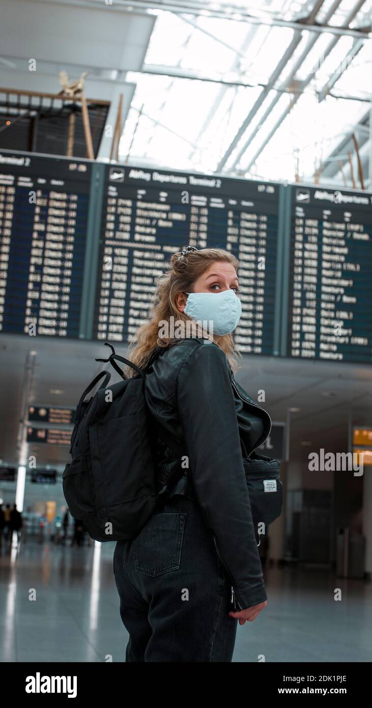 Junge blonde Frau am Flughafen München mit Mund-Nasen-Maske / Corona-Reise / Fluggast mit Schutzmaske Stockfoto