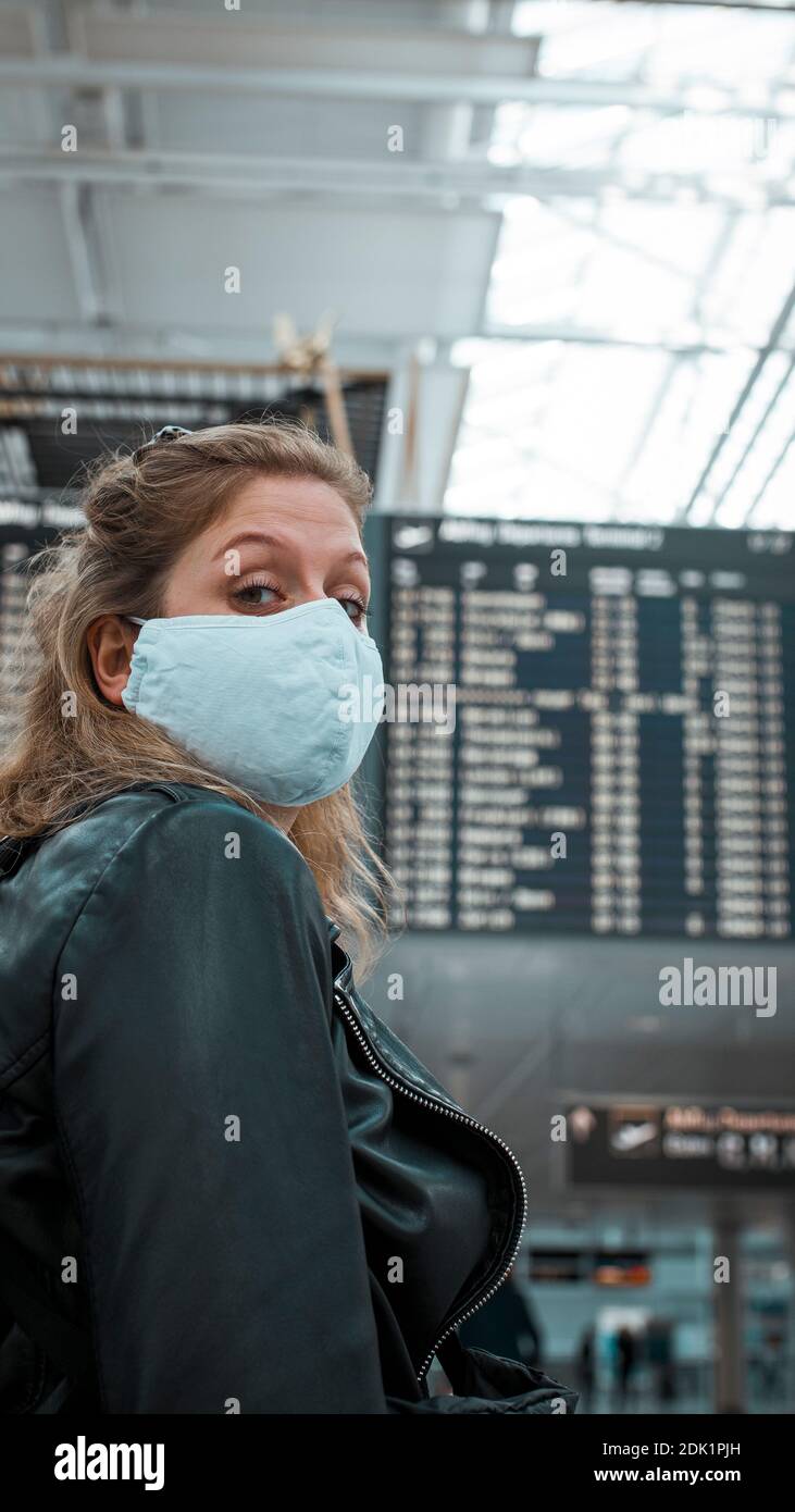Junge blonde Frau am Flughafen München mit Mund-Nasen-Maske / Corona-Reise / Fluggast mit Schutzmaske Stockfoto
