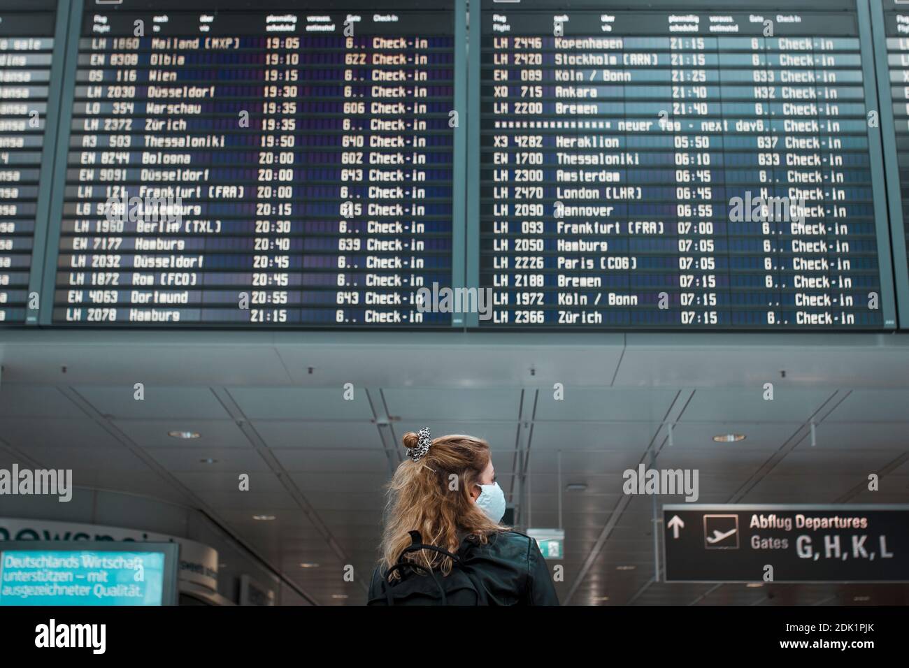 Junge blonde Frau am Flughafen München mit Mund-Nasen-Maske / Corona-Reise / Fluggast mit Schutzmaske Stockfoto