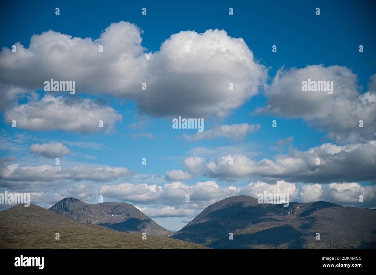 A beautiful landscape of the mountains gleaming under the fluffy cloudy blue sky Stockfoto