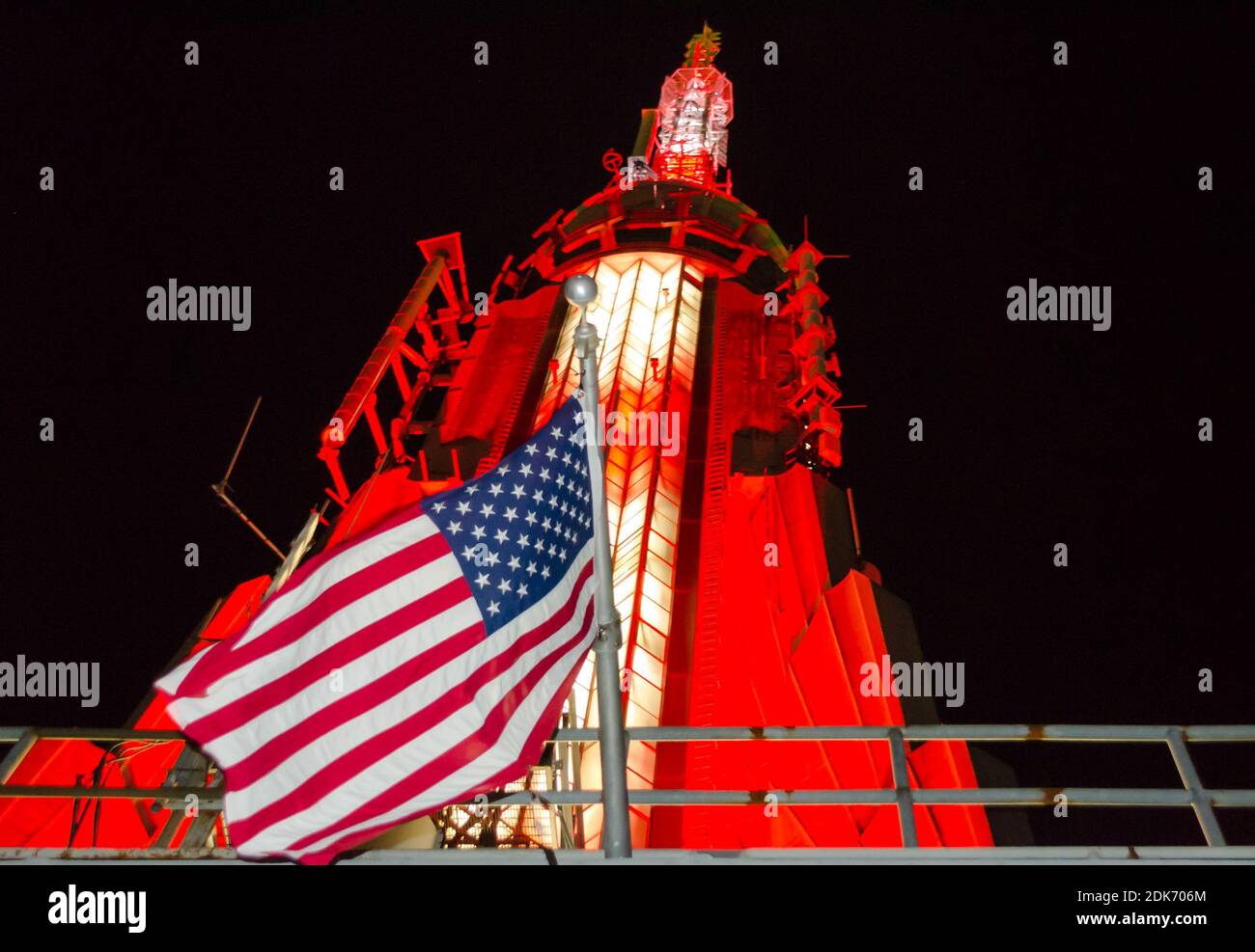 Low Angle View of Empire State Building Illuminated Antenna in der oberen Ebene des historischen Wolkenkratzers. Kultige Building Top mit der amerikanischen Flagge Stockfoto