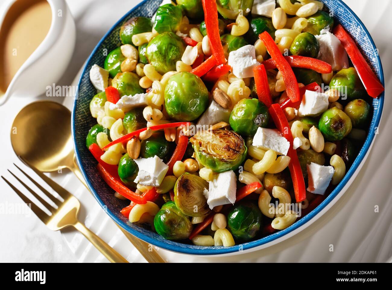 Makkaroni-Salat mit Brokkoli-Sprossen, Paprika-Streifen, Feta und Erdnuss in einer Schüssel mit Erdnusssauce auf einem Marmortisch, horizontale Ansicht von oben, c Stockfoto