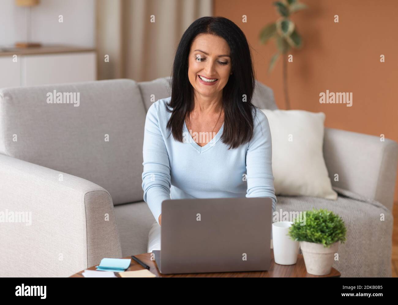 Reife Frau sitzt auf dem Sofa und arbeitet am Computer Stockfoto