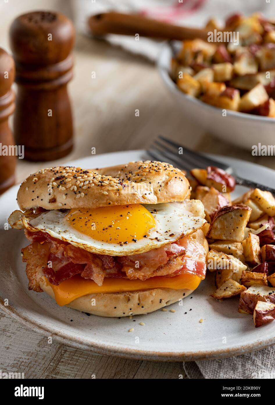 Bagel-Frühstückssandwich mit Spiegelei, Speck und Cheddar-Käse mit Bratkartoffeln auf einem Teller Stockfoto