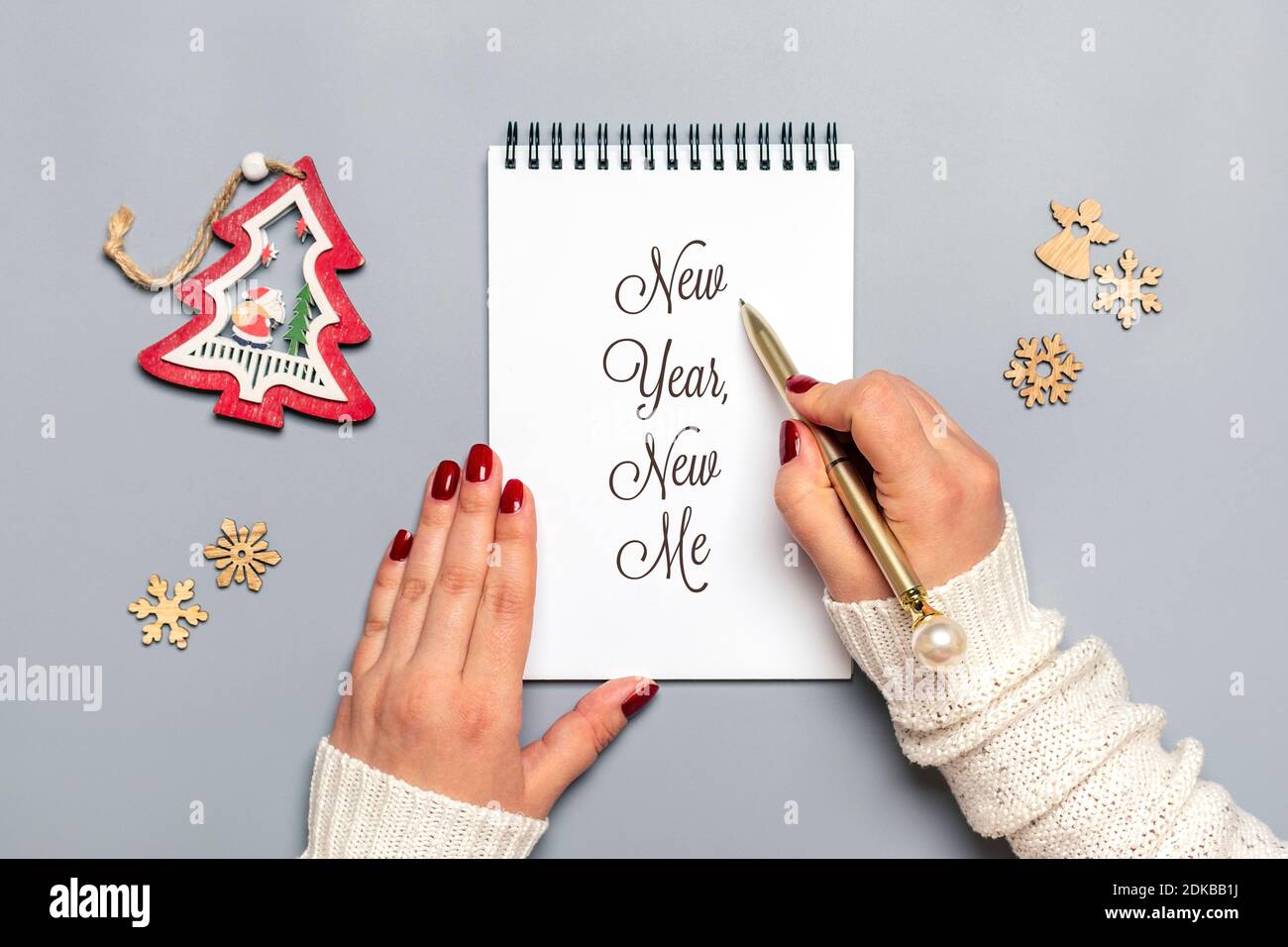 Weibliche Hand hält Stift und schreibt Neujahr, New Me auf weißem Notizblock, Baum, Schneeflocke auf grauem Hintergrund Draufsicht Flat Lay Geschäftsmotivation, Idee Stockfoto