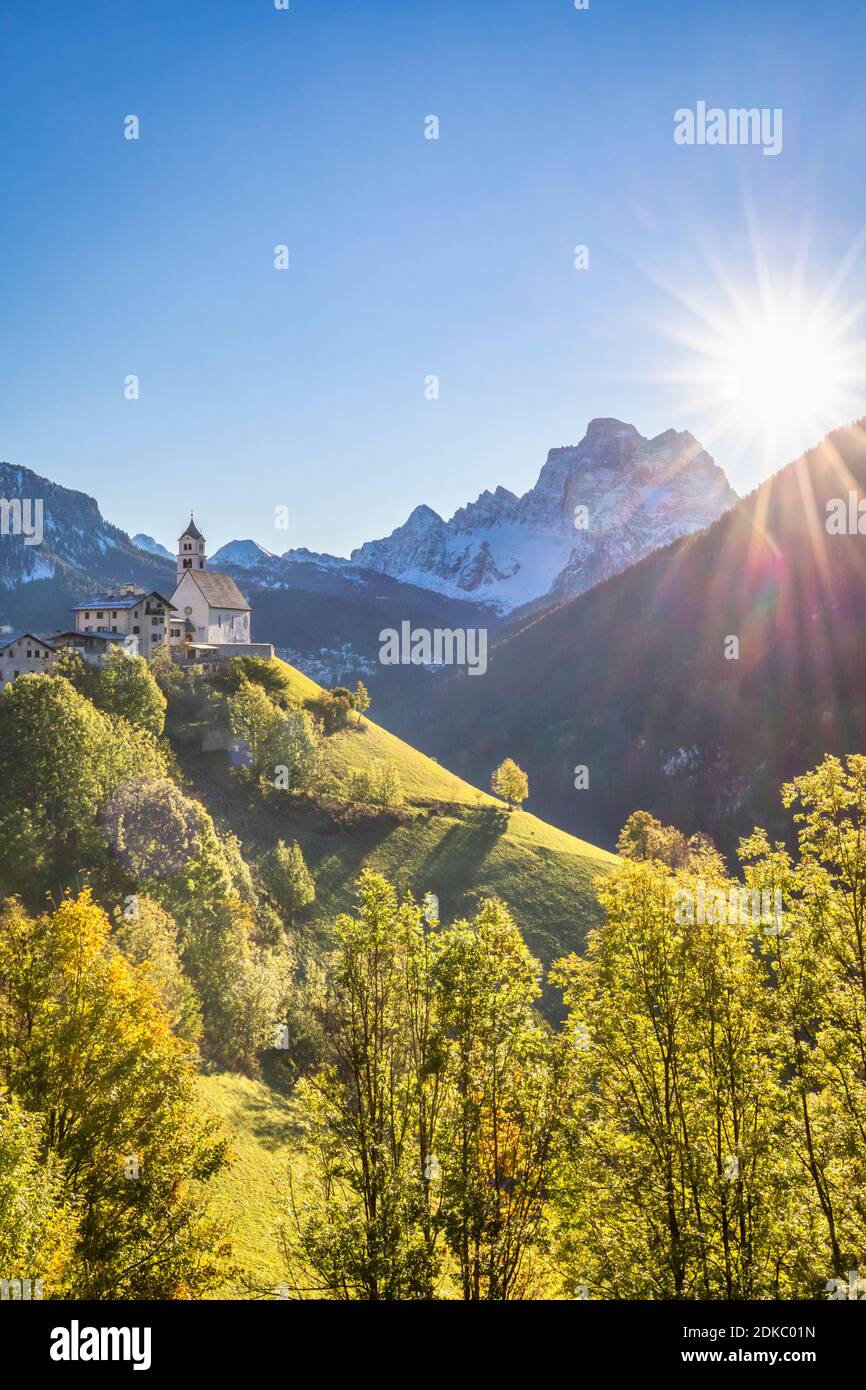 Ein klassischer Blick auf das Dorf Colle Santa Lucia dominiert von der Pfarrkirche und Monte Pelmo im Hintergrund, Herbstszene mit der Sonne am Himmel, Agordino, Provinz Belluno, Venetien, Italien, Europa Stockfoto