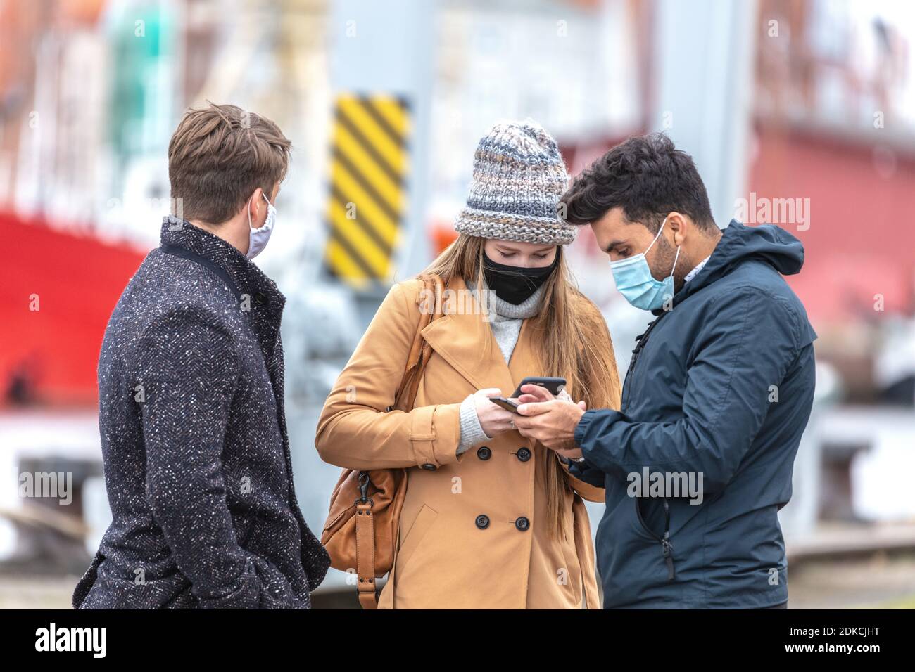 Zwei Männer und eine Frau mit Alltagsmasken in der Corona-Zeit, in der kalten Jahreszeit in der Stadt, Stockfoto