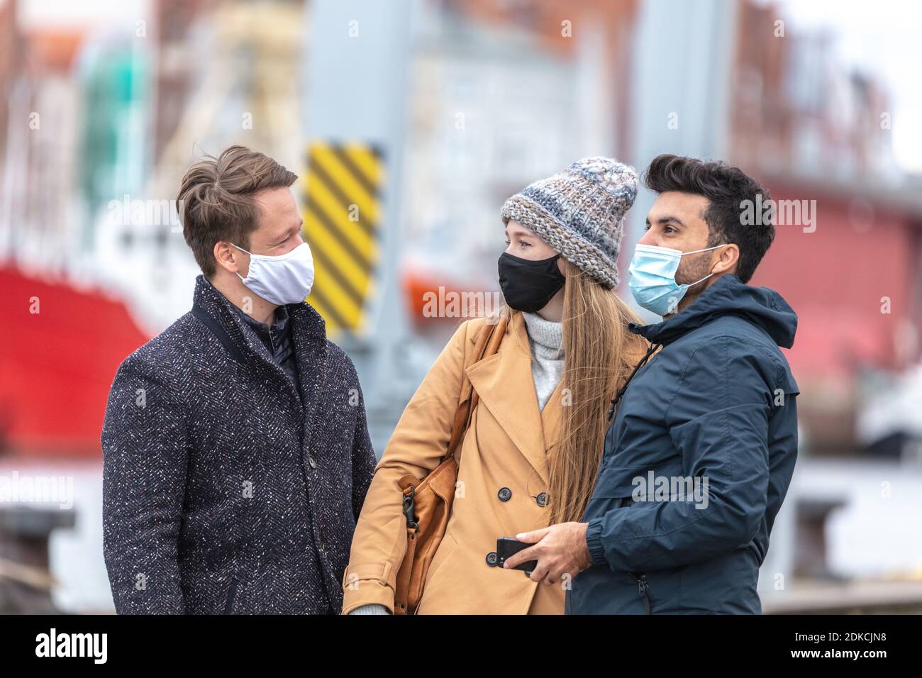 Zwei Männer und eine Frau mit Alltagsmasken in der Corona-Zeit, in der kalten Jahreszeit in der Stadt, Stockfoto