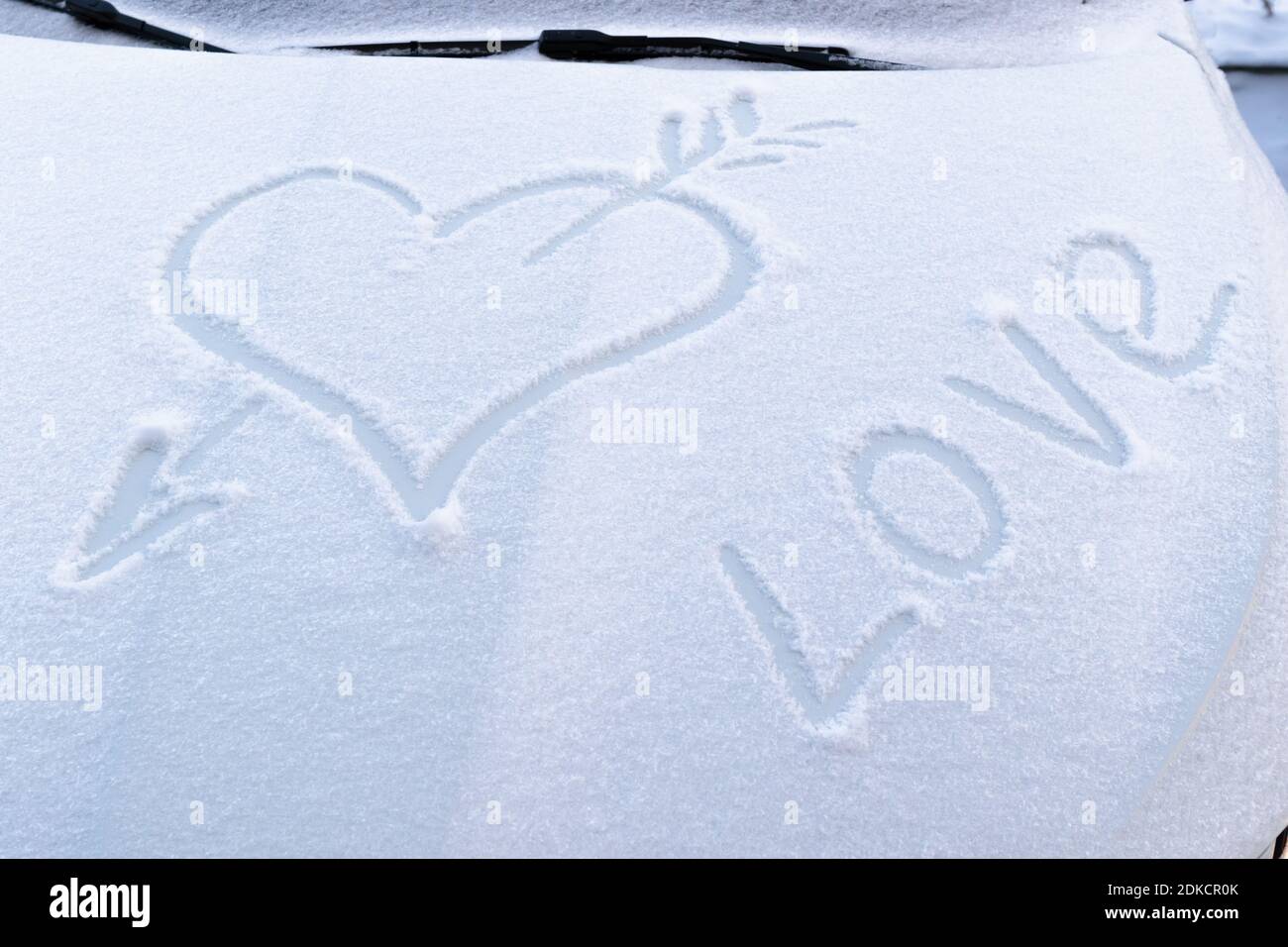 Bild eines gebrochenen Herzens mit einem Pfeil im Schnee auf der Motorhaube eines Autos auf einem frostigen Wintertag Stockfoto