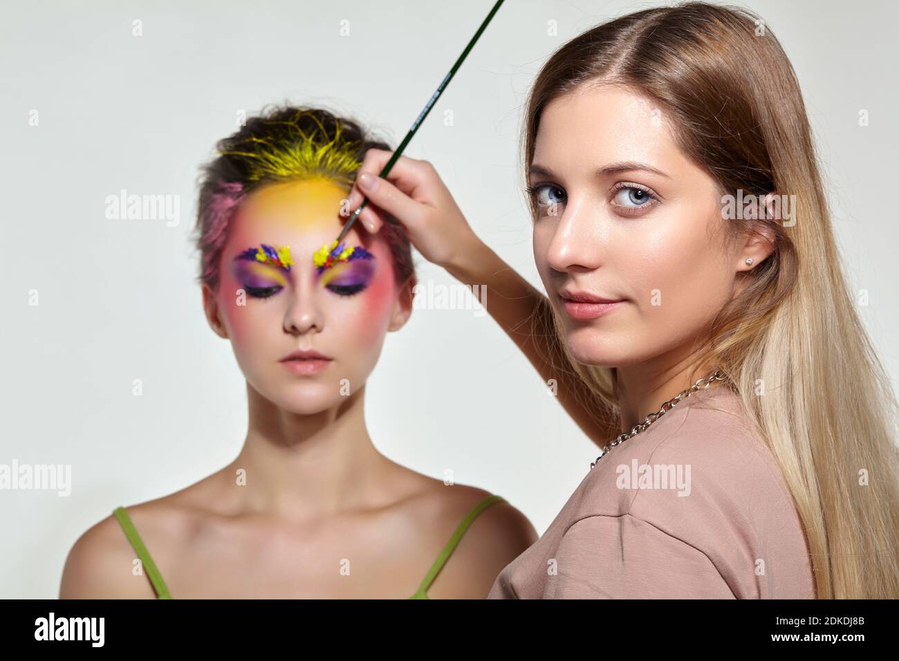 Weibliche Porträt mit ungewöhnlichen Gesicht Kunst Make-up. Farbe auf Augenbrauen, Haare und um die Augen. Künstler Hand mit Pinsel Malerei schöne Mädchen Brauen machen Stockfoto
