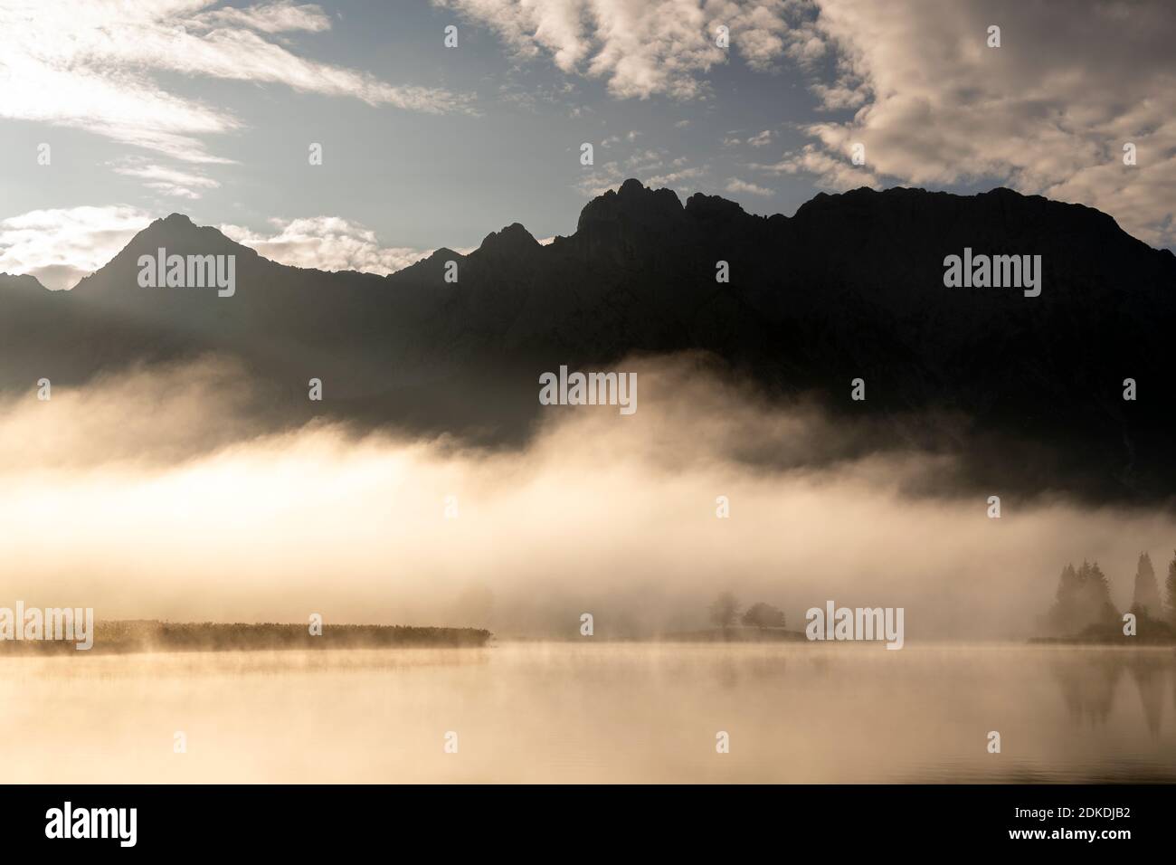 Herbststimmung an einem kleinen See in den bayerischen Alpen, im Hintergrund das Karwendelgebirge, eine kleine Halbinsel im Nebel und die Spiegelung im Wasser. Die neblige Atmosphäre mit den zerklüfteten Bergen hat eine fast mystische Wirkung. Stockfoto