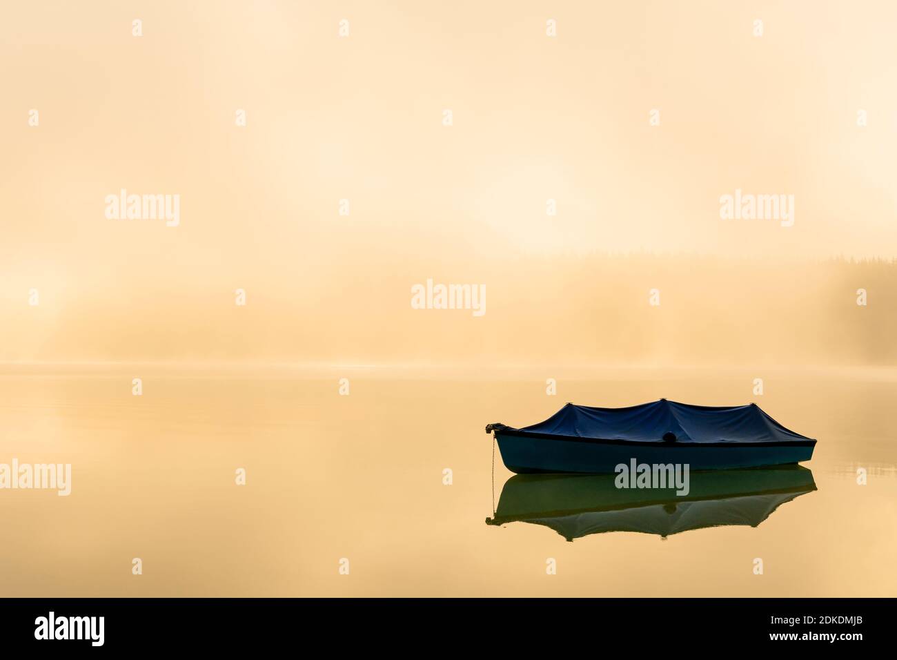 Ruderboot mit Plane auf dem Sylvensteinspeichersee im Karwendelgebirge. Im Hintergrund Nebel bei Sonnenaufgang mit einer einzigartigen Lichtatmosphäre und ruhiges Wasser. Stockfoto