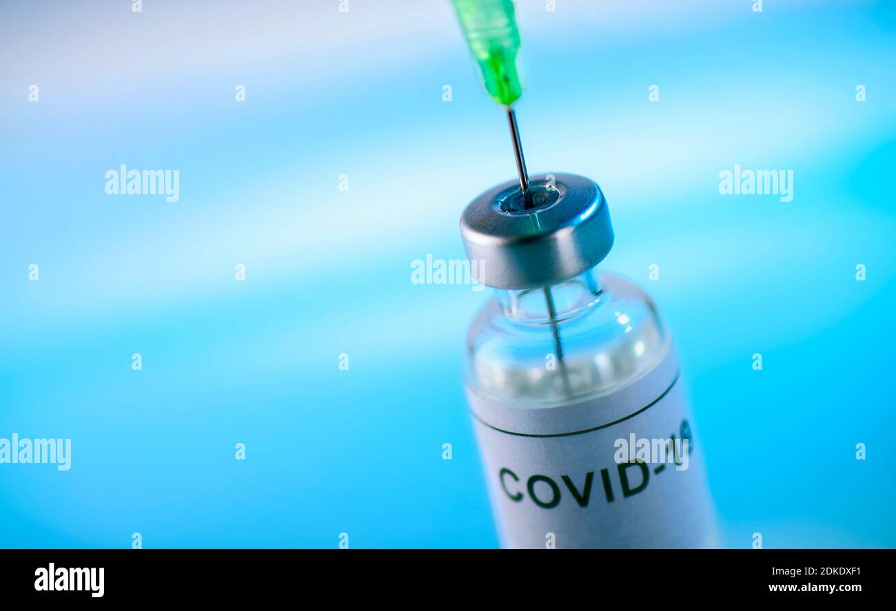 Injektionsmaterial mit der Aufschrift Covid-19 und der Nadel von Eine Spritze vor blauem Hintergrund Stockfoto