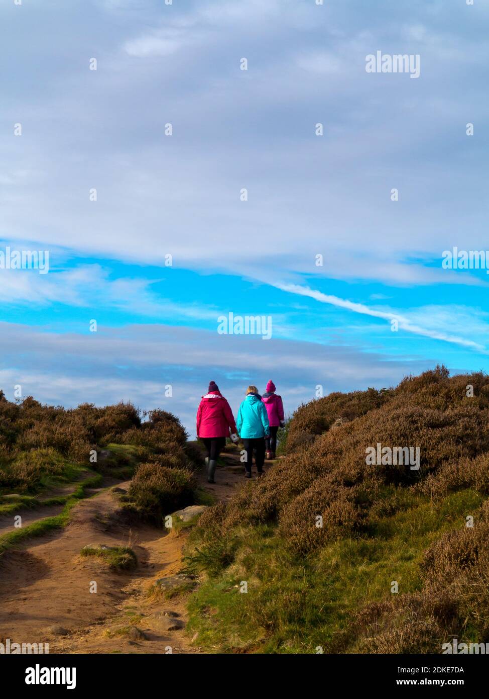 Rückansicht von drei Personen, die auf einem Moorpfad bei Wintersonne mit blauem Himmel und Wolken wandern. Stockfoto
