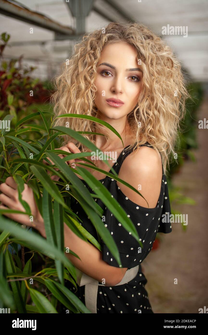 Porträt eines schönen jungen Mädchen, das zwischen grünen Pflanzen steht Blick auf die Kamera und lächeln Stockfoto