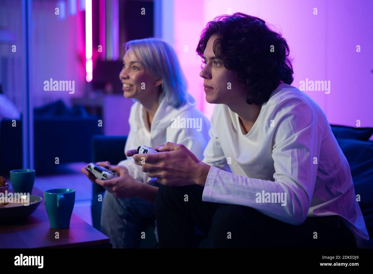 Ein paar junge Erwachsene spielen Videospiele zu Hause. Emotionale diverse Gamer halten Joysticks und konkurrieren in intensiven Videospiel auf Spielkonsole. Stockfoto