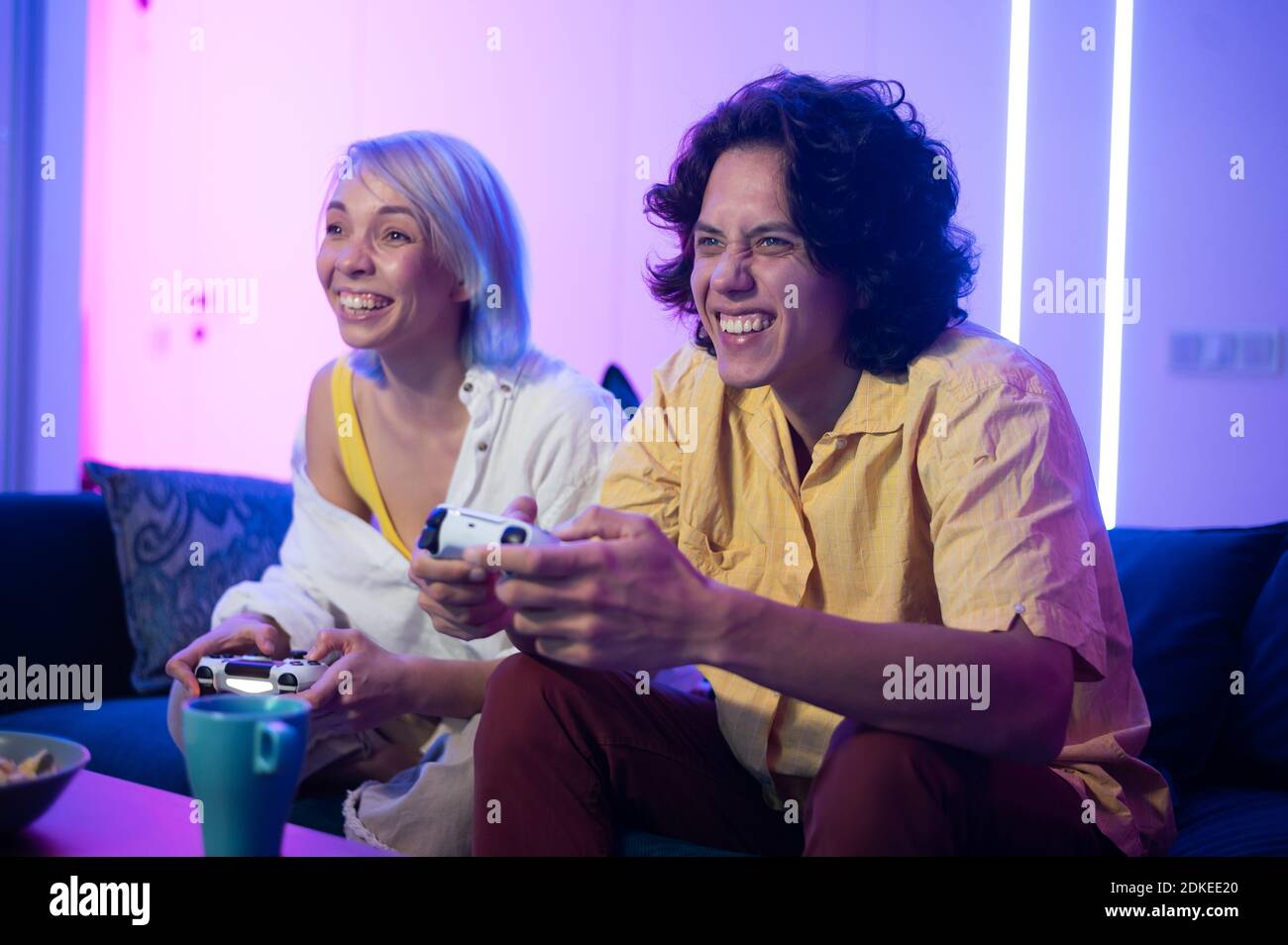 Glücklich Freund und Freundin spielen Videospiele und halten Joysticks zu Hause. Millennial Paar genießen Spiel, während auf dem Sofa sitzen und Ausgaben Stockfoto