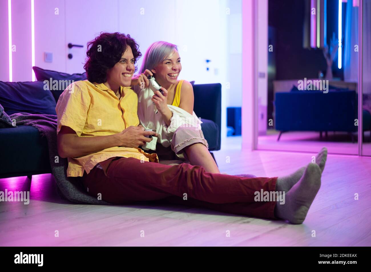 Junges Paar spielen Videospiele, während auf dem Wohnzimmer Boden mit Neonfarbe beleuchtet sitzen. Stockfoto