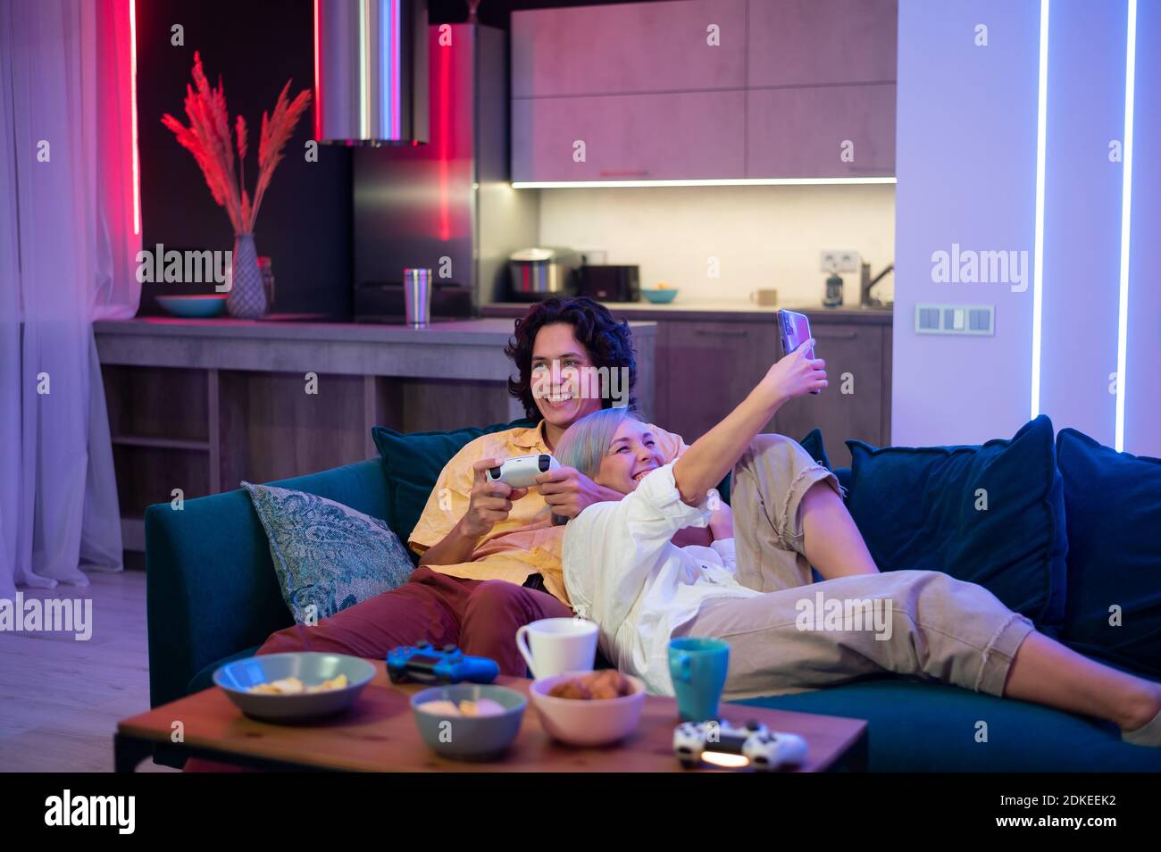 Guy spielt Videospiel, während Mädchen mit Smartphone für soziale Medien. Verbringen Sie Zeit zusammen zu Hause. Stockfoto