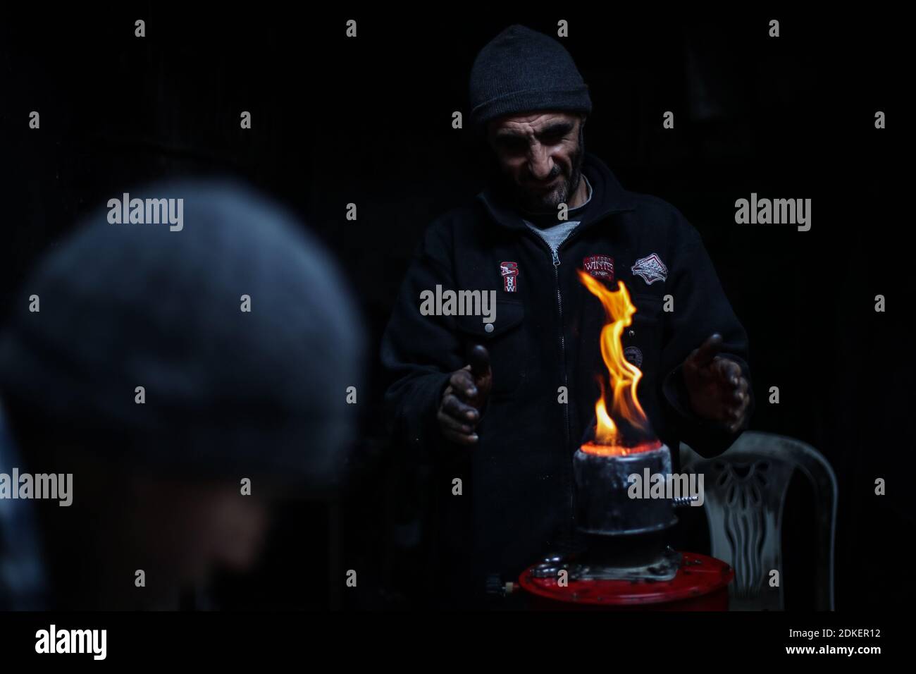 Ariha, Syrien. Dezember 2020. Ein syrischer Mann verwendet eine gasbetriebene Heizung, um seine Hände bei kühlen Wetterbedingungen auf einem lokalen Markt zu wärmen. Das vom Krieg zerrissene Syrien erlebt sehr heiße Sommer und ebenso kalte Winter, was große Probleme für diejenigen verursacht, die zur Binnenvertreibung gezwungen wurden. Quelle: Anas Alkharboutli/dpa/Alamy Live News Stockfoto