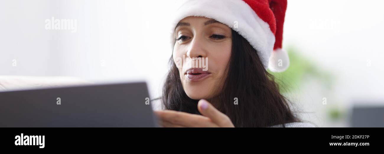 Frau in santa claus Hut lächelt und Schläge Kuss zu Laptop-Computer Stockfoto