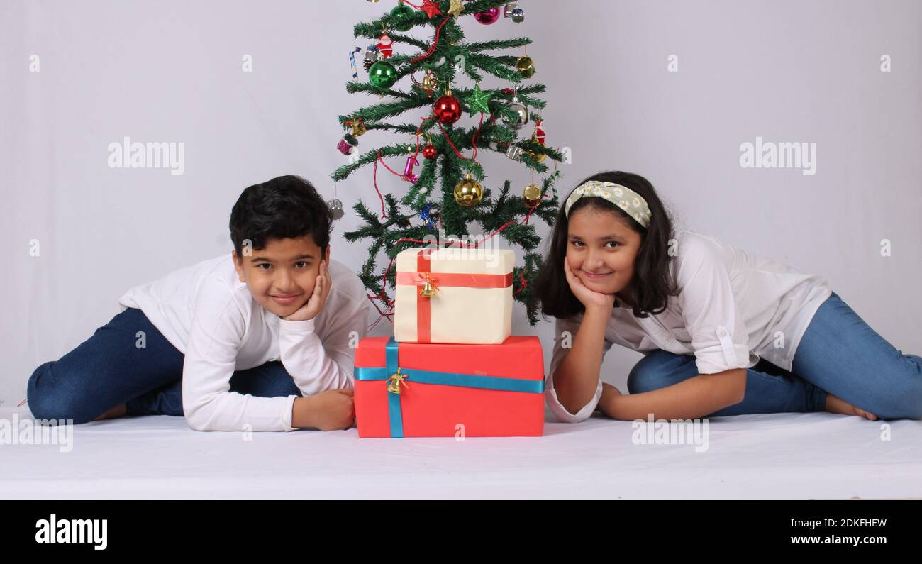 Nette kleine indische Kinder feiern weihnachten zu Hause mit Weihnachtsmütze, Geschenke und Weihnachtsbaum Stockfoto