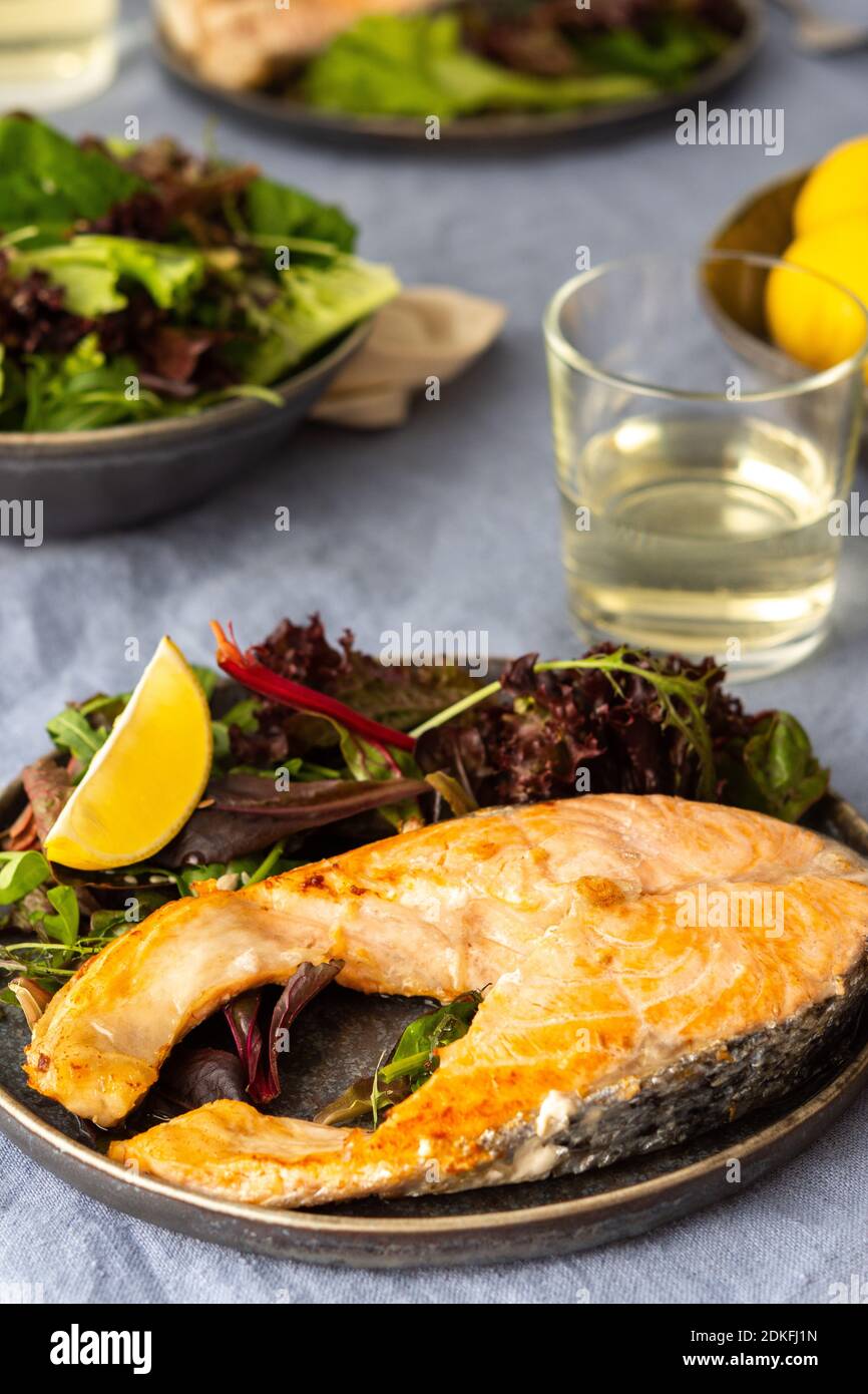 Gebratenes Lachssteak mit Salat auf einem Teller, Weißwein im Glas, leckeres herzhaftes Abendessen oder Mittagessen Stockfoto