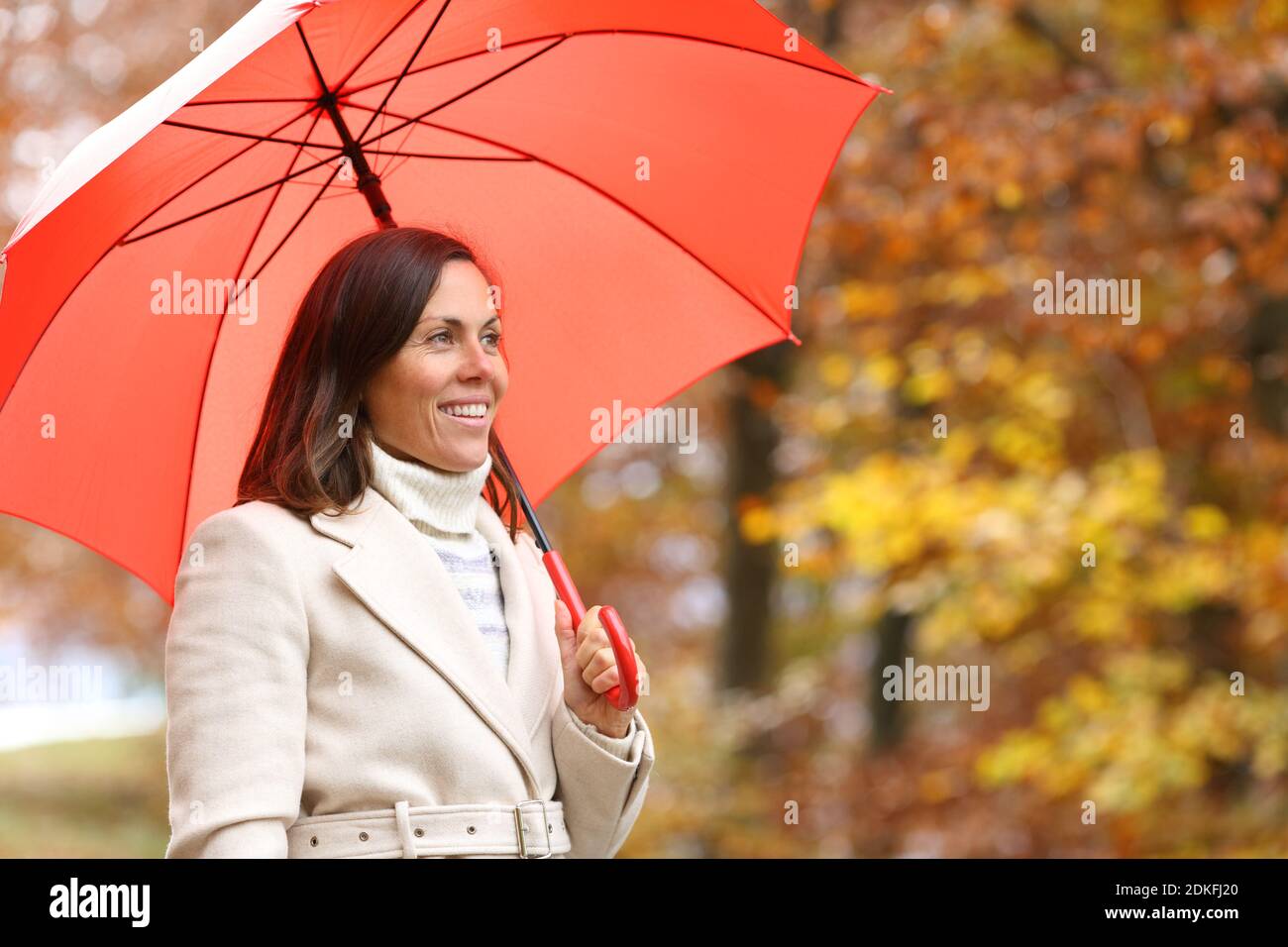 Glückliche Erwachsene Frau erwägt Herbst unter rotem Regenschirm in einem parken Stockfoto