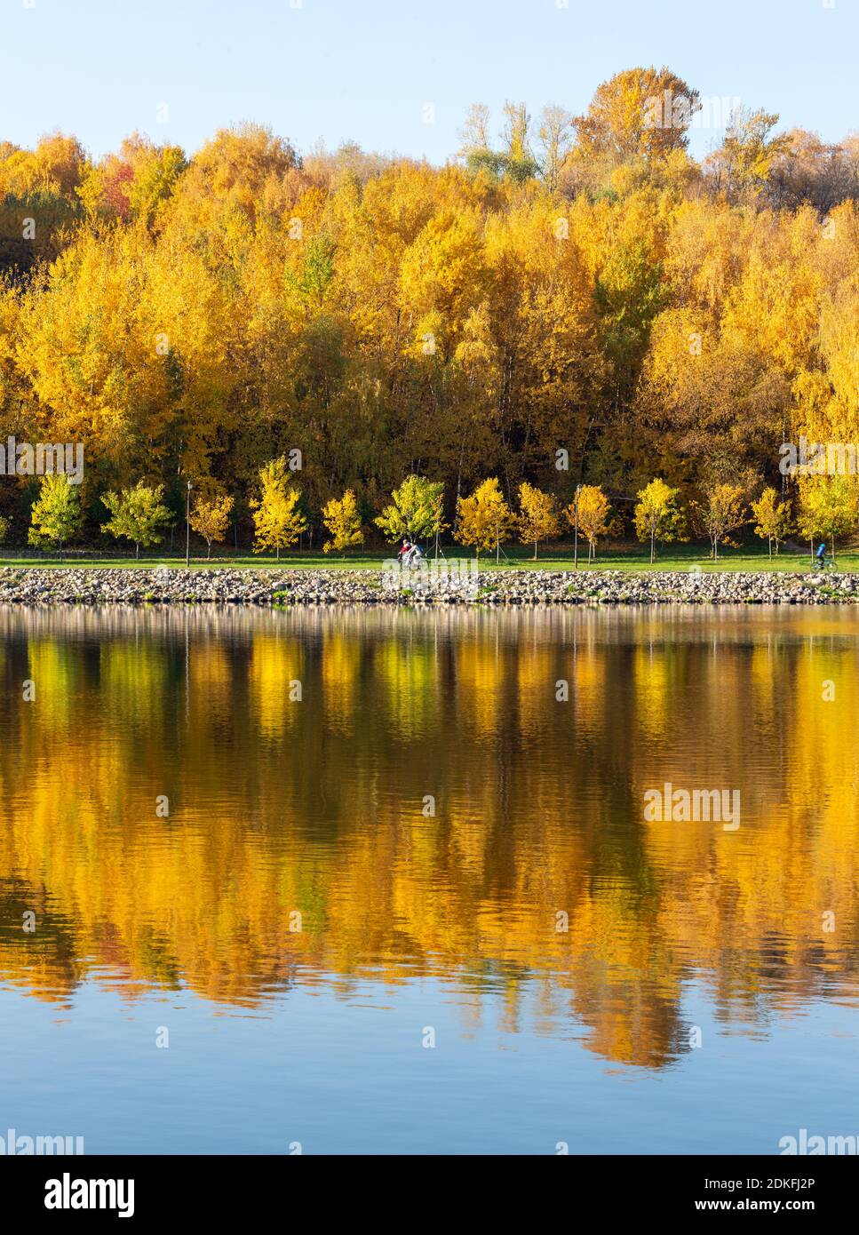 Farbenfroher Herbst. Gasse am Flussufer entlang auf dem Hintergrund des Herbstparks bei sonnigem Herbsttag. Reflexionen im Wasser des Waldes und blauen s Stockfoto