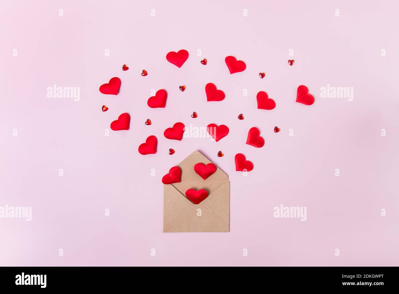 Rote Herzen fliegen aus Bastelpapier-Umschlag auf hellrosa Hintergrund. Valentinstag. Liebeskonzept. Geschenk, Nachricht für Liebhaber. Leerzeichen für Text. Stockfoto
