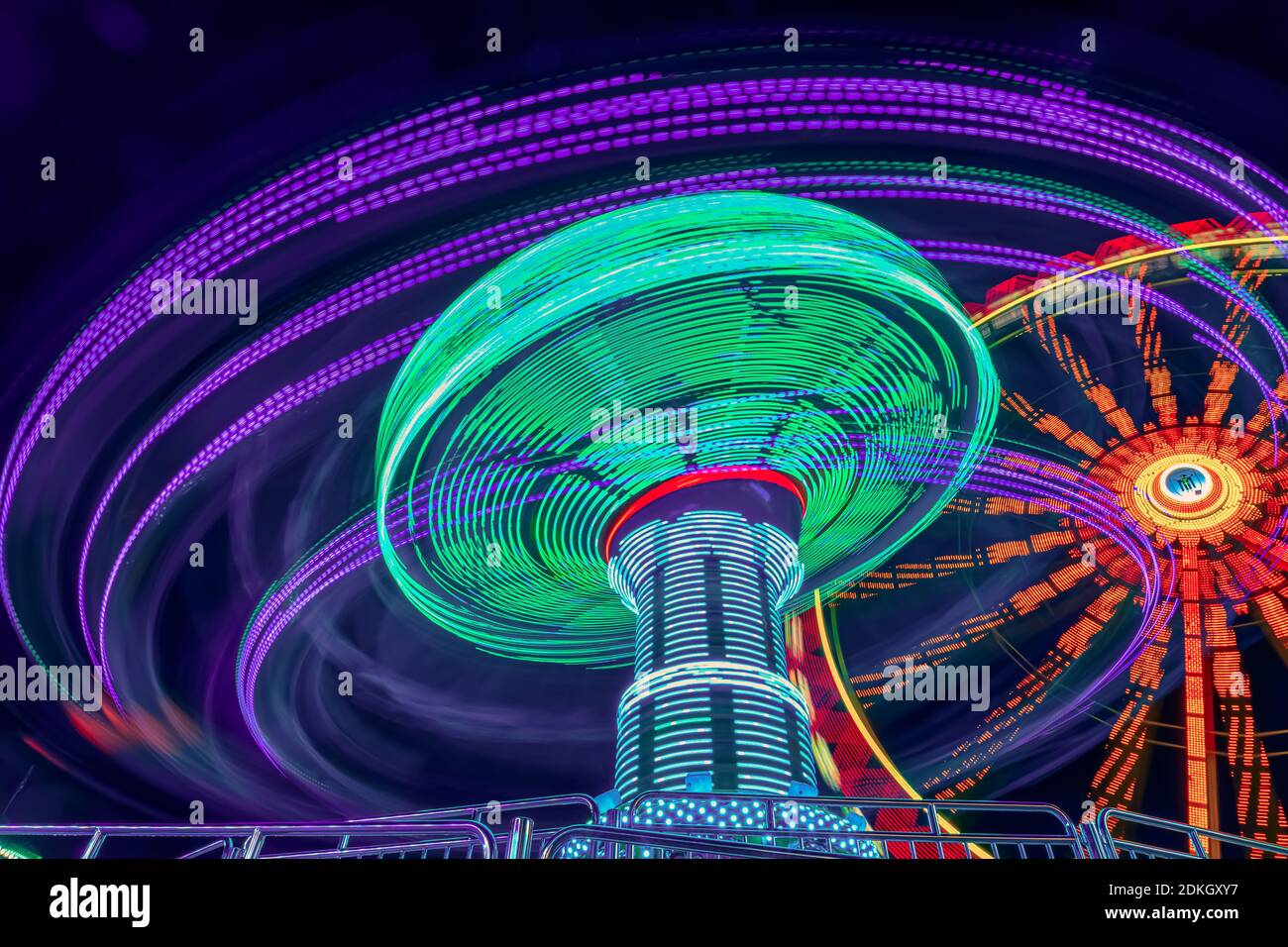 Spaß für Jugendliche und Gruppen von Freunden und auch eine Familie. Eine lange Exposition eines Vergnügungsparks mit einem Kettenkarusel in einer sehr dynamischen Rotation, bunte Lichter in den späten Stunden des Tages Stockfoto