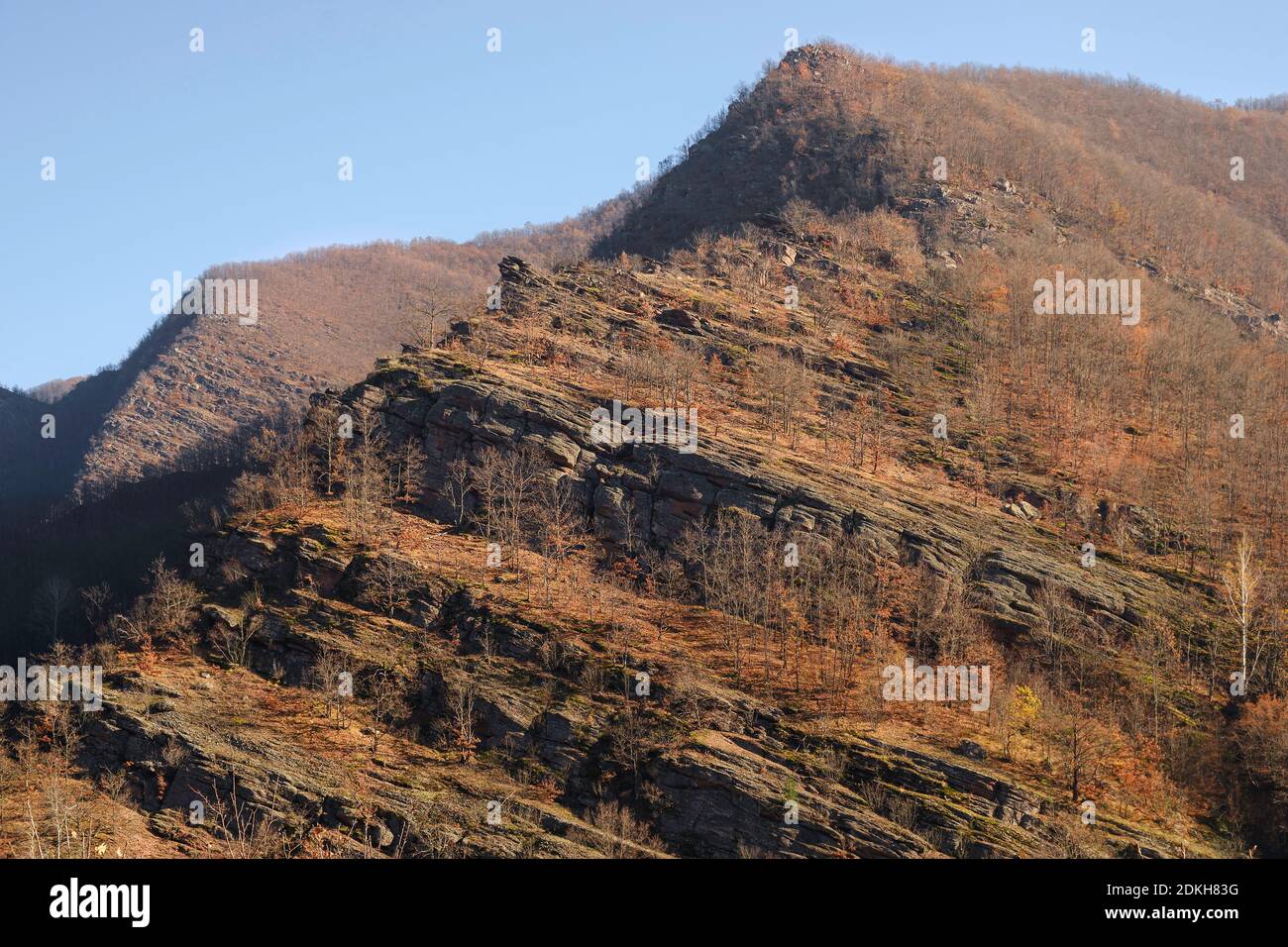 Spitzige Spitze, steile, geschichtete Klippen, bedeckt von herbstbunten Bäumen und klarem blauen Himmel Stockfoto