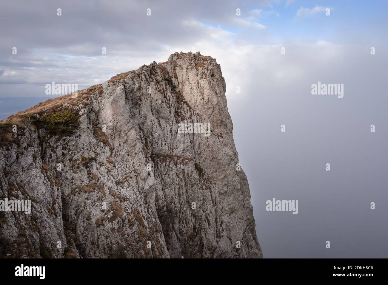 Felsige, steile, senkrechte Klippe auf dem trockenen Berg (Suva planina) bedeckt mit trockenem, orangefarbenem Gras im Herbst und wolkenblauem Himmel Stockfoto