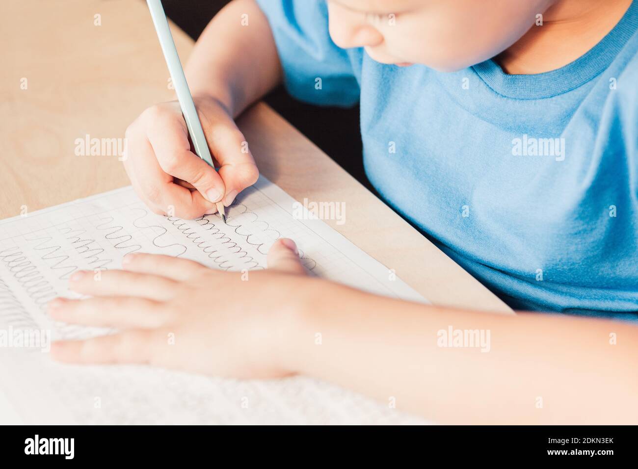 Schule Kind tun schriftlich Aufgabe zu Hause. Kind zeichnet Linien mit Bleistift. Vorschreiben Übung, um die Hand für Schreiben Briefe vorzubereiten Stockfoto