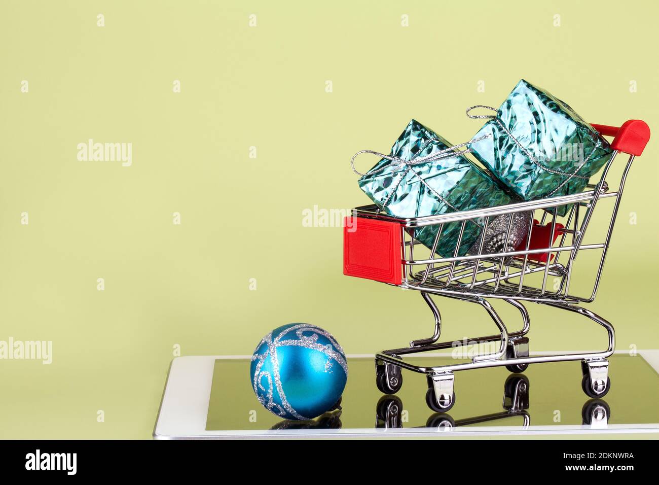 Online, Urlaub einkaufen. Supermarkt Trolley mit Geschenkboxen, Tablet-pc und Weihnachtskugel auf grünem Hintergrund. Platz kopieren Stockfoto