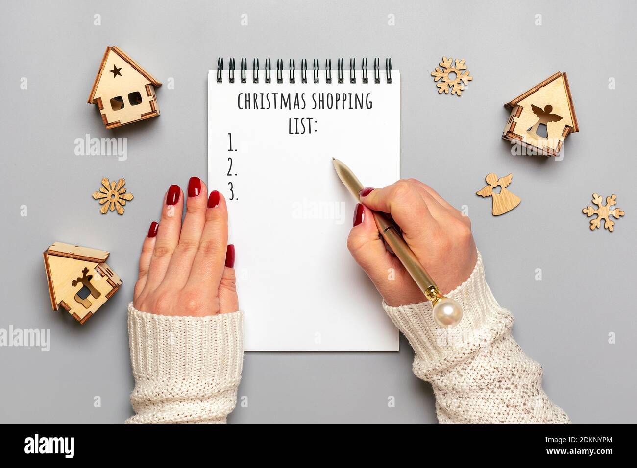 Weibliche Hand hält Stift, schreiben Weihnachtseinkaufsliste, Geschenkideen auf weißem Notizblock auf grauem Hintergrund Draufsicht Flat Lay Weihnachtskarte Frau macht Chr. Stockfoto