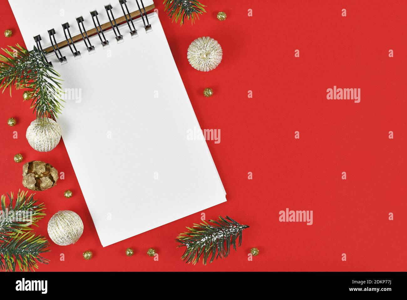 Weißes leeres Notizbuch, umgeben von Weihnachtsdekoration in der Ecke Roter Hintergrund mit leerem Kopierbereich Stockfoto