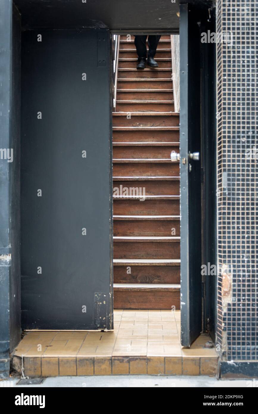 Eine offene graue Tür mit umlaufenden Fliesen, mit einer sodden Treppe sichtbar und die Beine einer Person zu Fuß nach unten Stockfoto