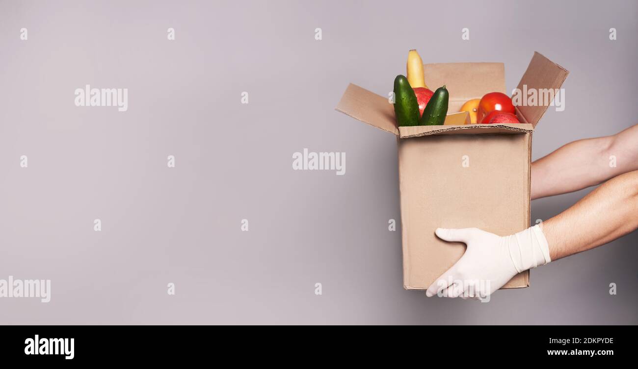 Hände von weißen Kurier in Gummihandschuhen halten einen Karton mit Lebensmitteln, schnelle und sichere Lieferung von Lebensmitteln. Stockfoto