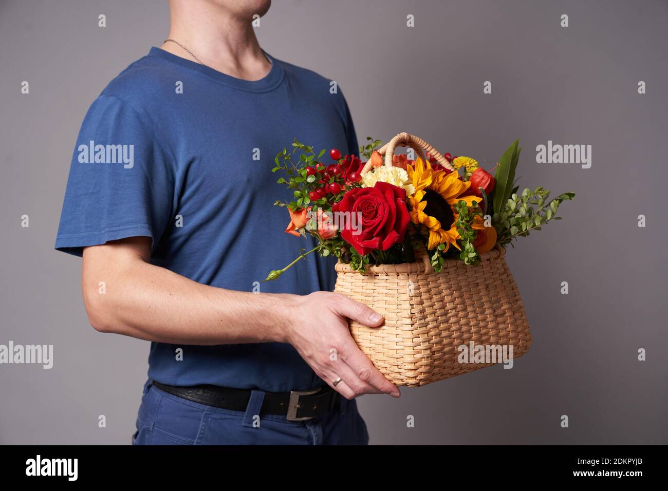 Ein weißer Mann in einem blauen T-Shirt hält einen Blumenkorb mit einem Kopierplatz auf einem grauen Hintergrund aus, Blumenlieferung Stockfoto