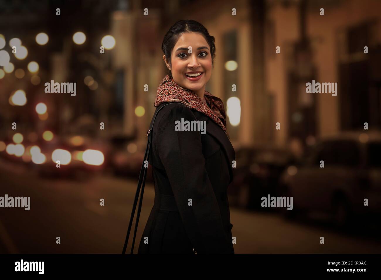 EINE JUNGE FRAU, DIE AUF EINER BELEBTEN STRASSE SMILNG STEHT KAMERA Stockfoto