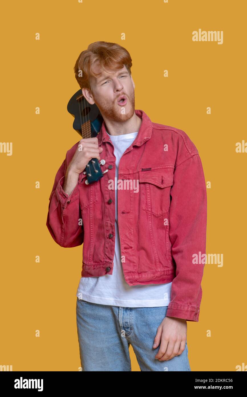 Junger bärtiger Mann in roter Jacke mit Ukulele Stockfoto