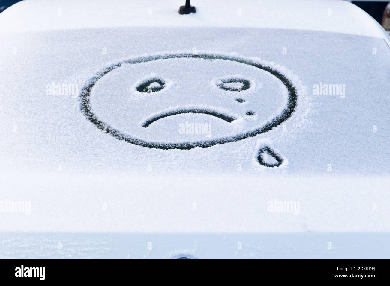 Bild eines weinenden Gesichts Emoji auf dem Schnee auf Das hintere Fenster eines Autos auf einem hellen frostigen Wintertag Stockfoto