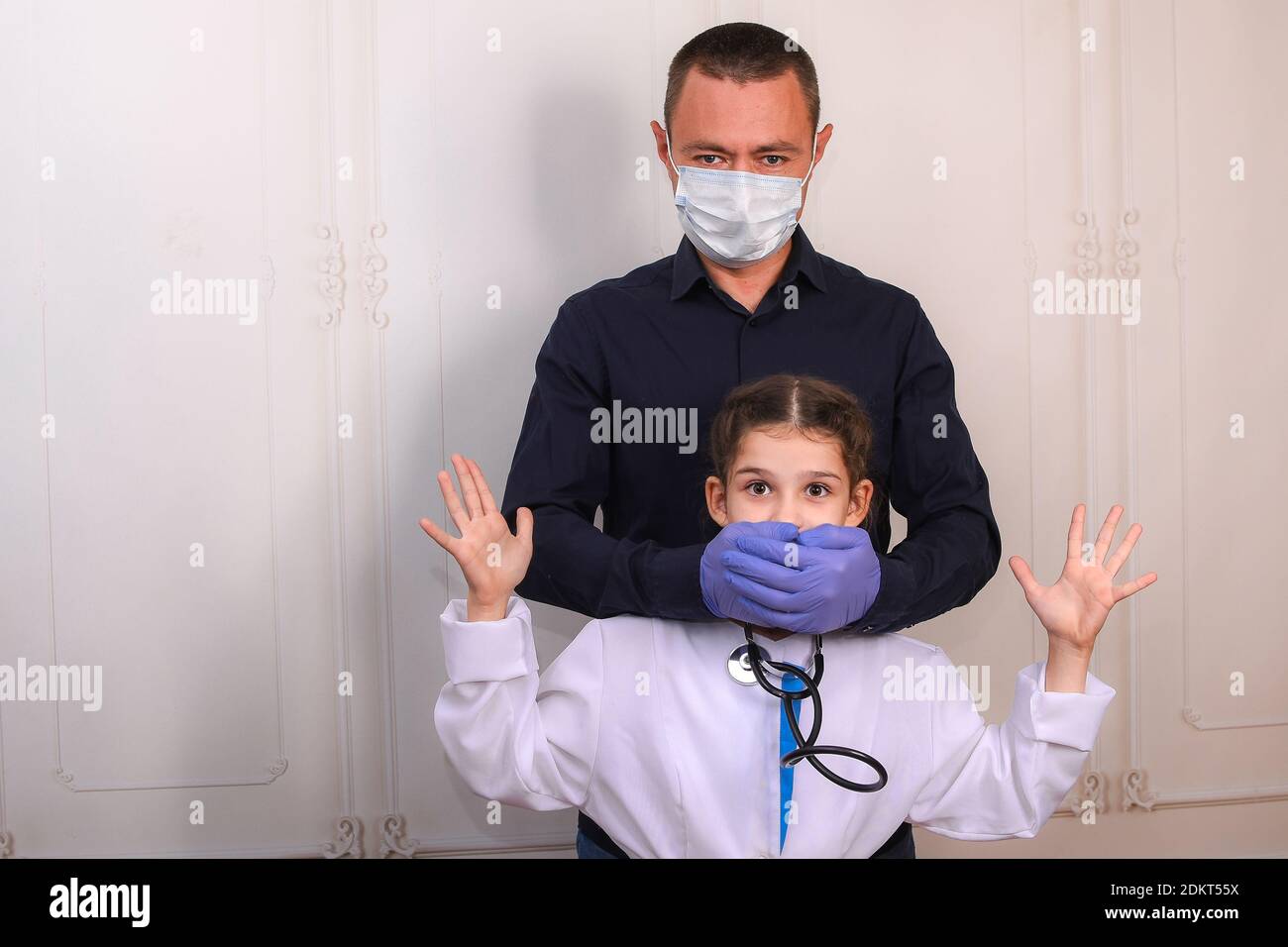 Nettes Mädchen 6-10 Jahre alt spielend mit Papa. Entzückendes Kind im medizinischen Labormantel mit einem Stethoskop vergaß, eine medizinische Maske anzuziehen. Ihr Vater verdeckte seine Stockfoto