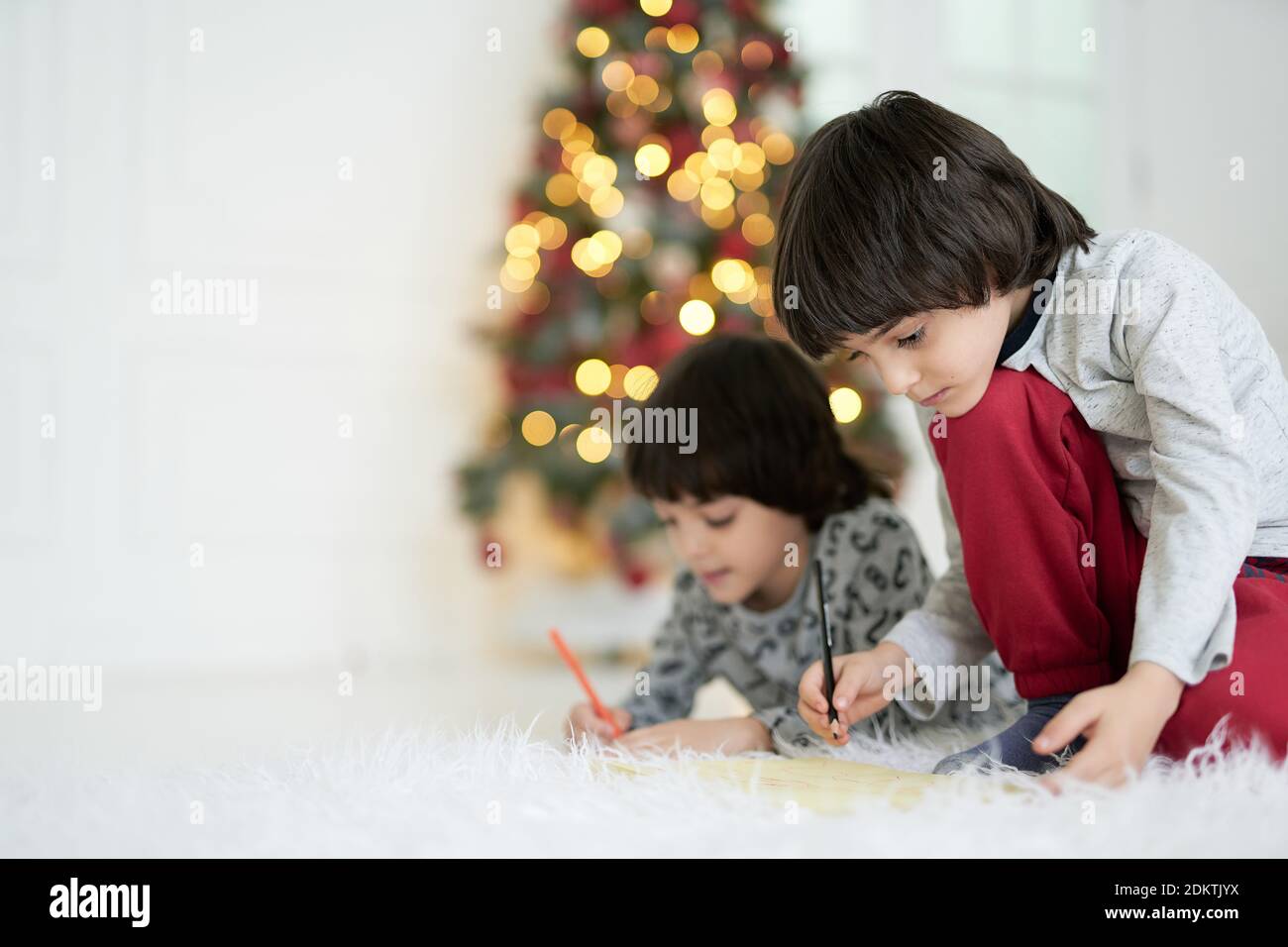 Zwei kleine lateinische Jungen, Zwillinge, die Bilder mit Bleistiften zeichnen, während sie zu Weihnachten auf dem Boden sitzen. Kindheit, Familie, Winterurlaub Stockfoto