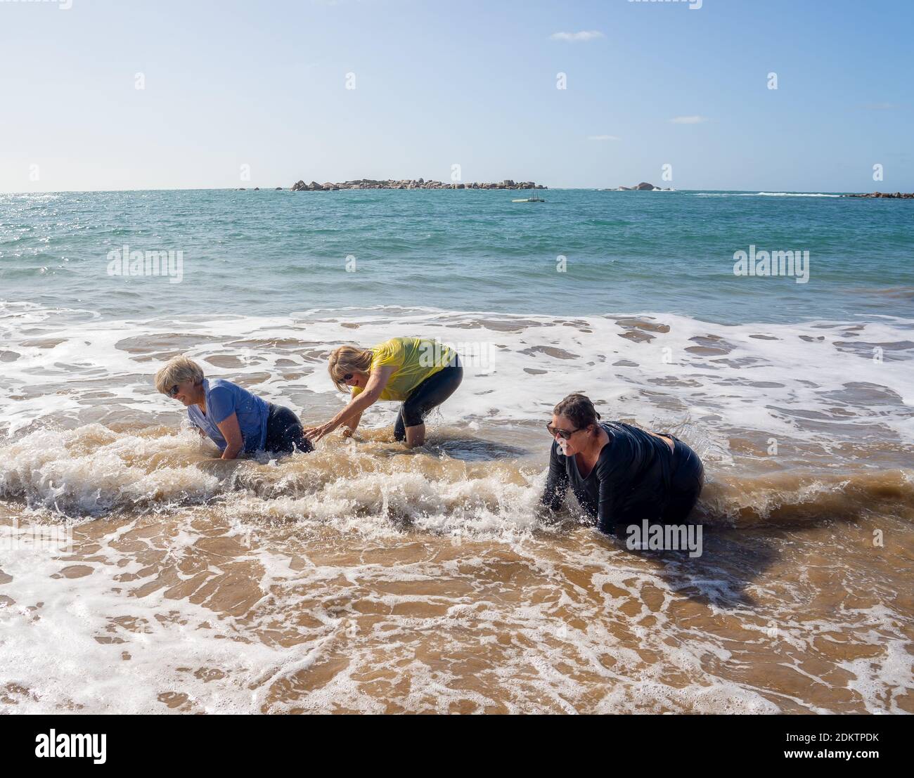 Gruppe von älteren Frauen im Ruhestand in den 60ern und 70ern, die im Wasser fallen und Spaß am Strand haben. Ältere Damen lachen, als sie fallen und verlieren Balan Stockfoto