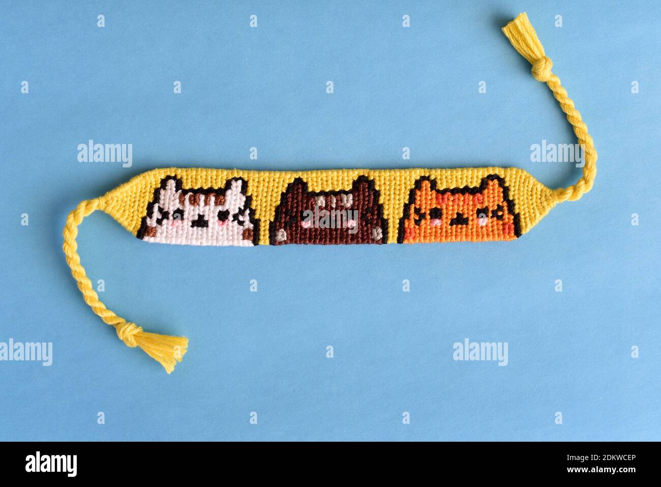 Gewebte DIY Freundschaft Armband mit Katzen-Muster handgefertigt von Stickerei Zahnseide auf blauem Hintergrund Stockfoto